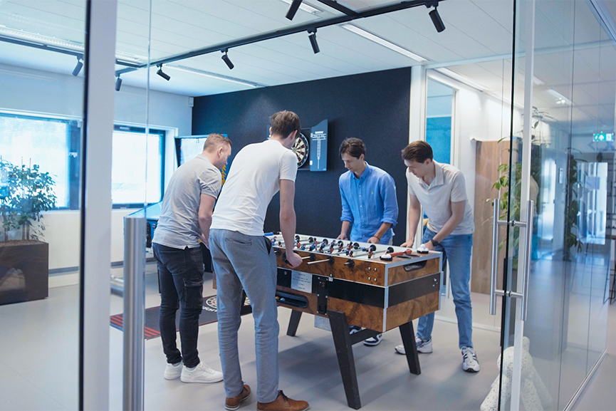 vier personen aan een tafelvoetbal tafel in een kantoorruimte 